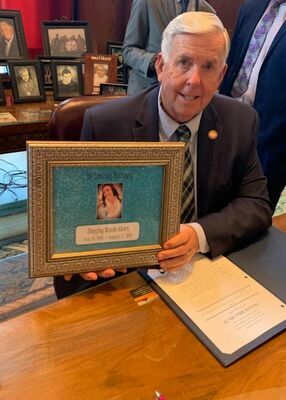 Missouri Governor Parson holding a picture of Shayley Akers. Shayley was the daughter of Lela Thompson. Lela lost her daughter to suicide.